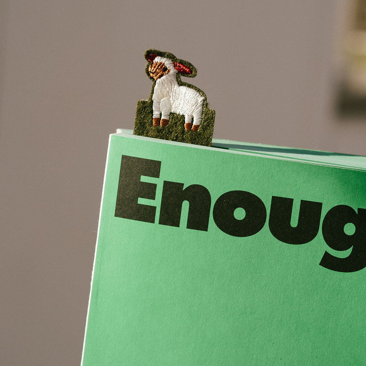 Sheep-shaped paper clip on a green book with 'Enough' text